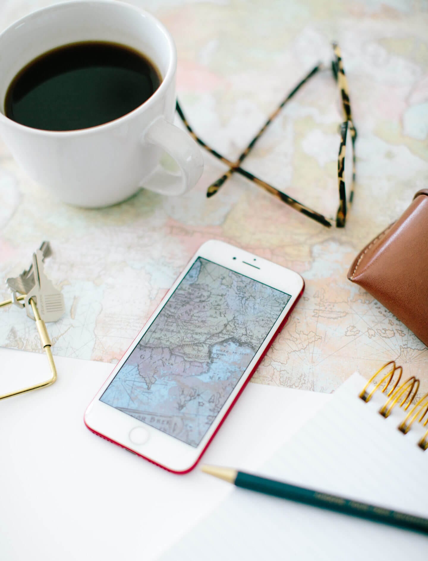 Someone travel planning with a map, iphone, glasses, notepad, and coffee. Is this person planning a trip with a travel agent or booking online?