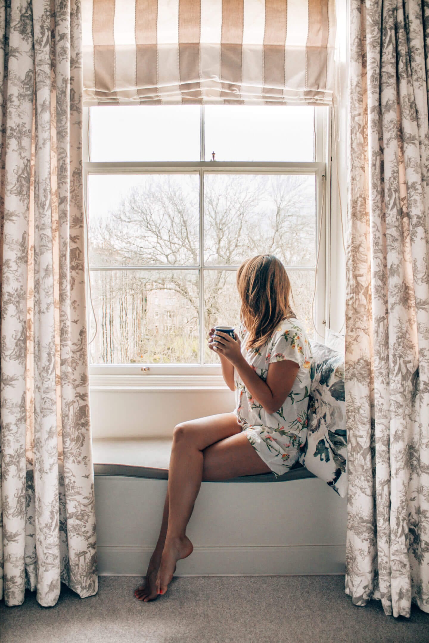 A girl sits in her pajamas sipping a cup of tea and admiring the beautiful views from her hotel room in Edinburg