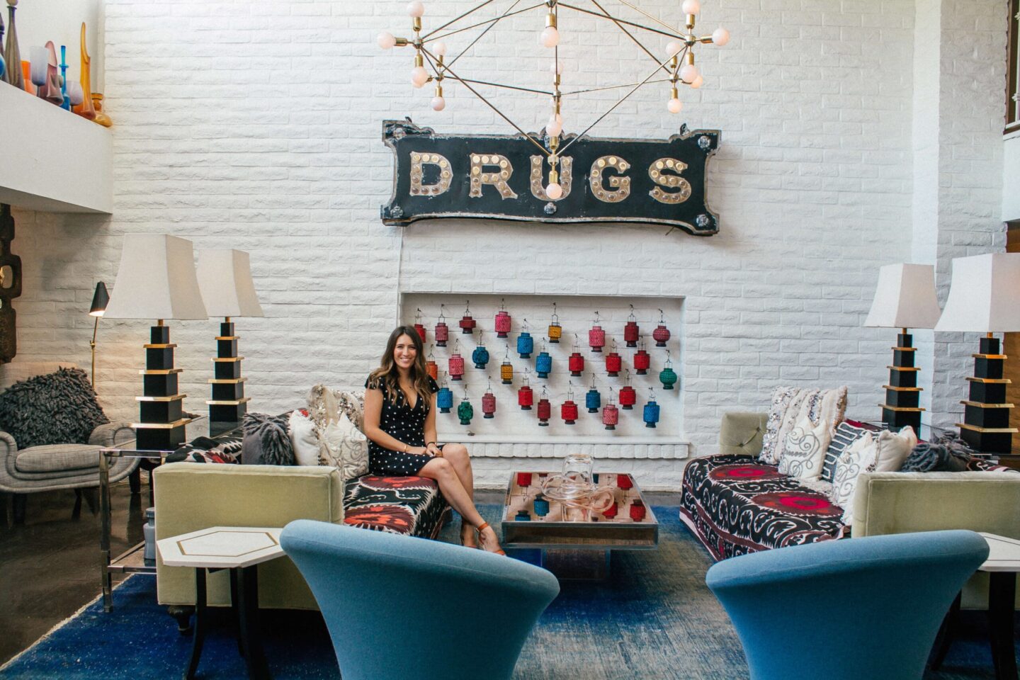 A girl sits in The Parker Palm Springs lobby underneath the 'Drugs' sign.