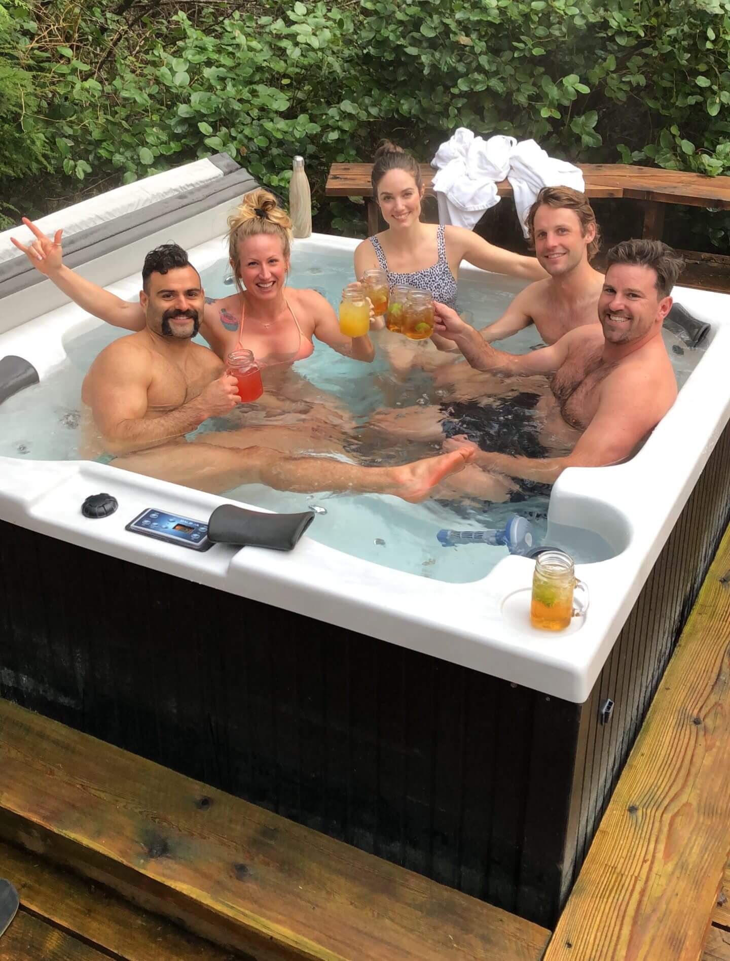 A group of young adults cheers drinks in a hot tub in Tofino, BC