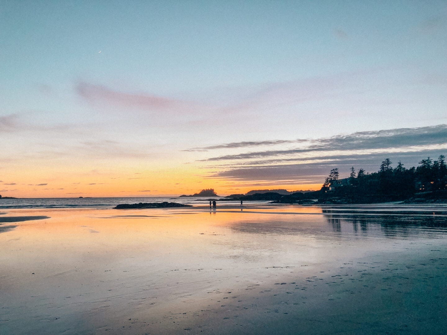 A yellow sunset in Tofino, BC reflections off the sand at the beach