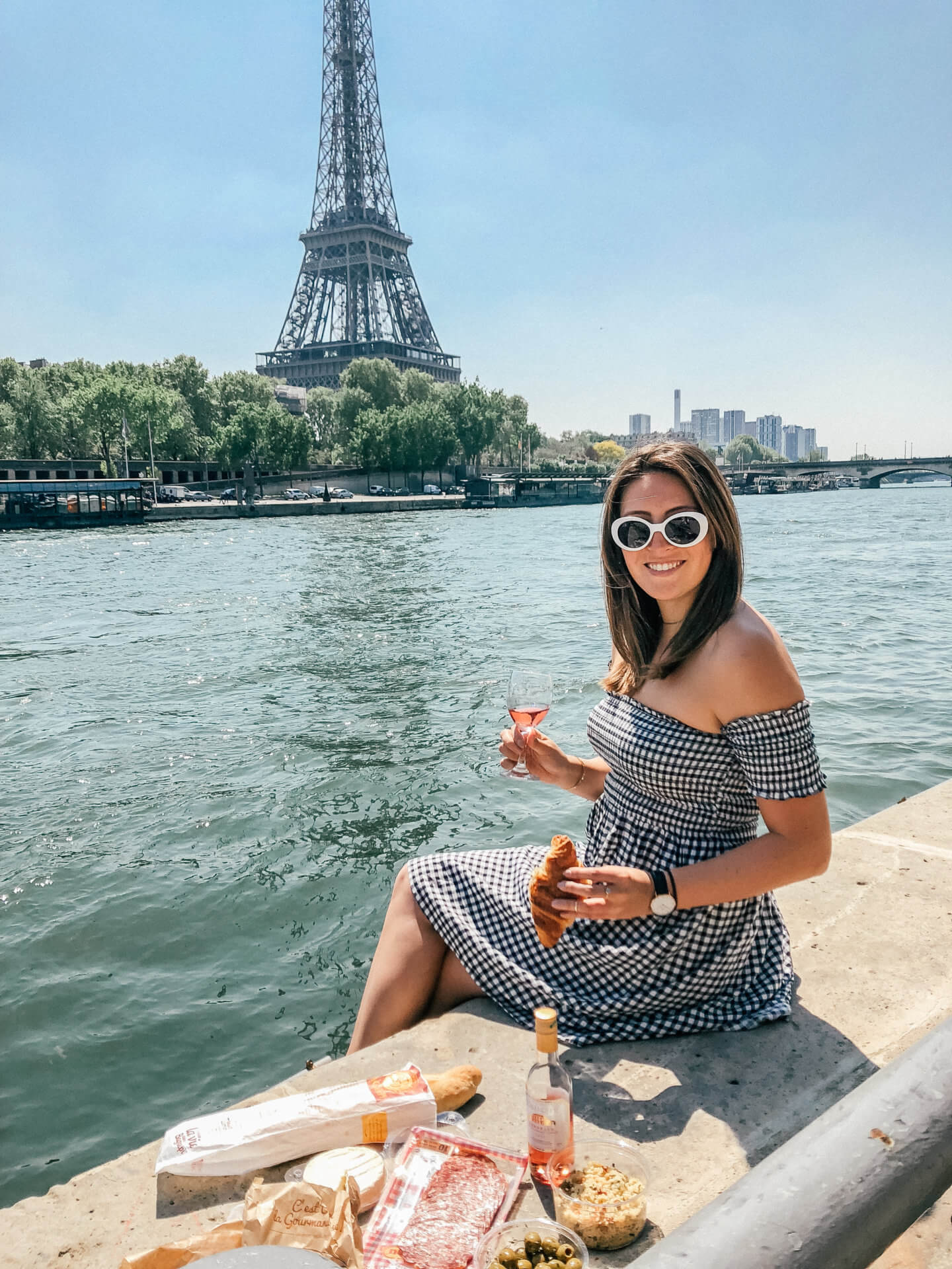 A girl holding a glass of rose and croissant in front of the Eiffel Tower in Paris - one of the most romantic places in Europe for a Unique Honeymoon