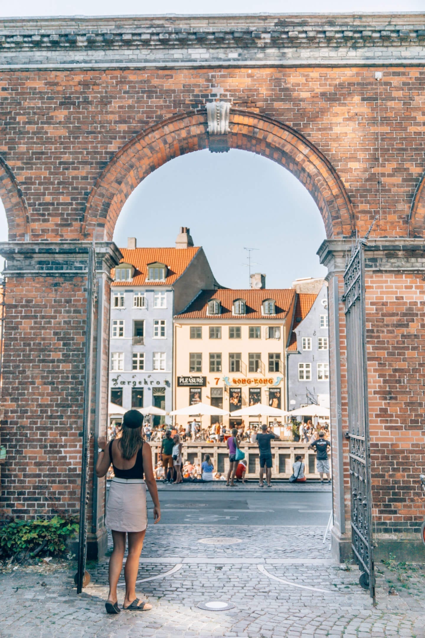 Girl with a hat standing in a brick archway looking at Nyhavn in Copenhagen