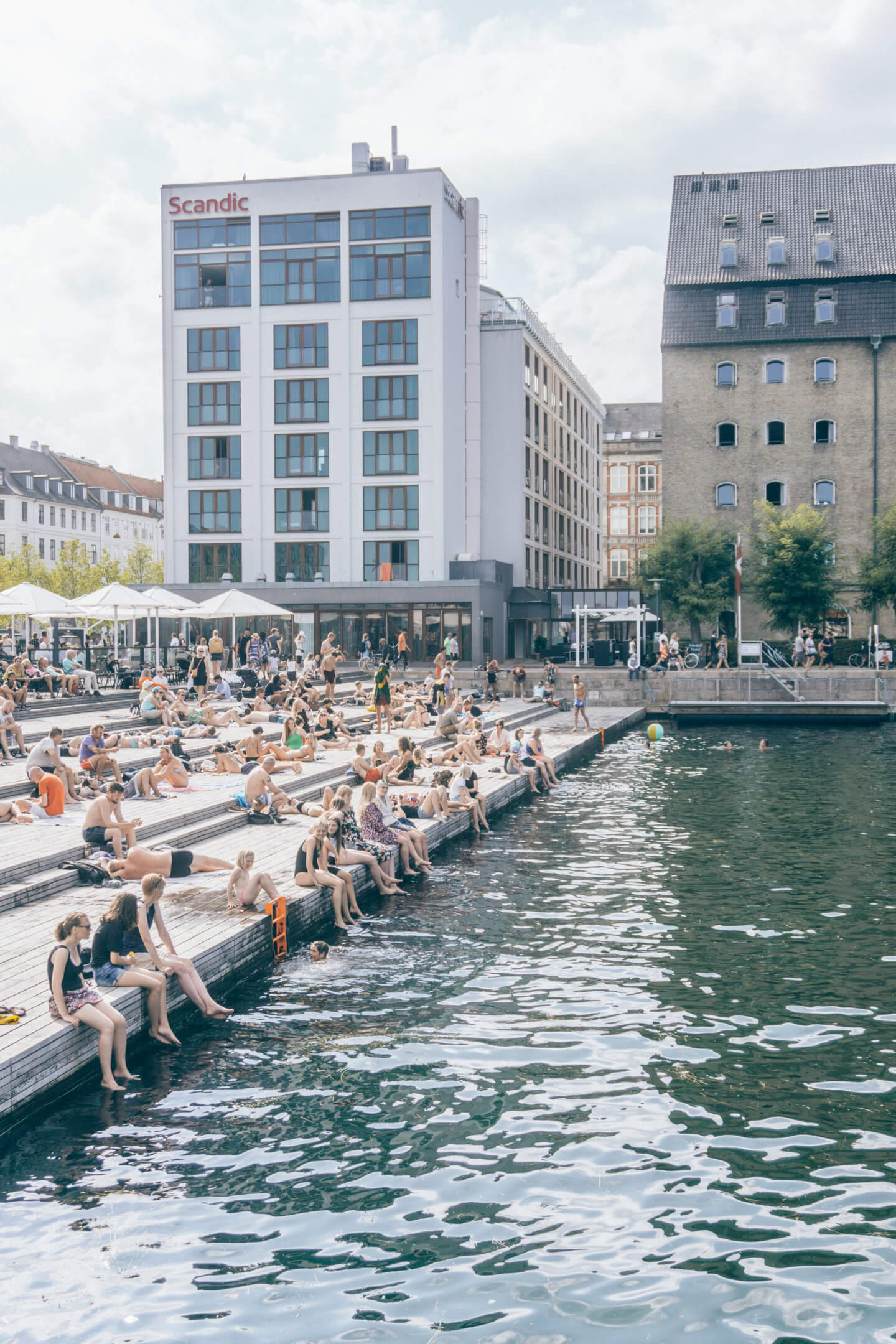 A group of people sitting with their feet dangling in the water of a Copenhagen canal during the heat of the summer