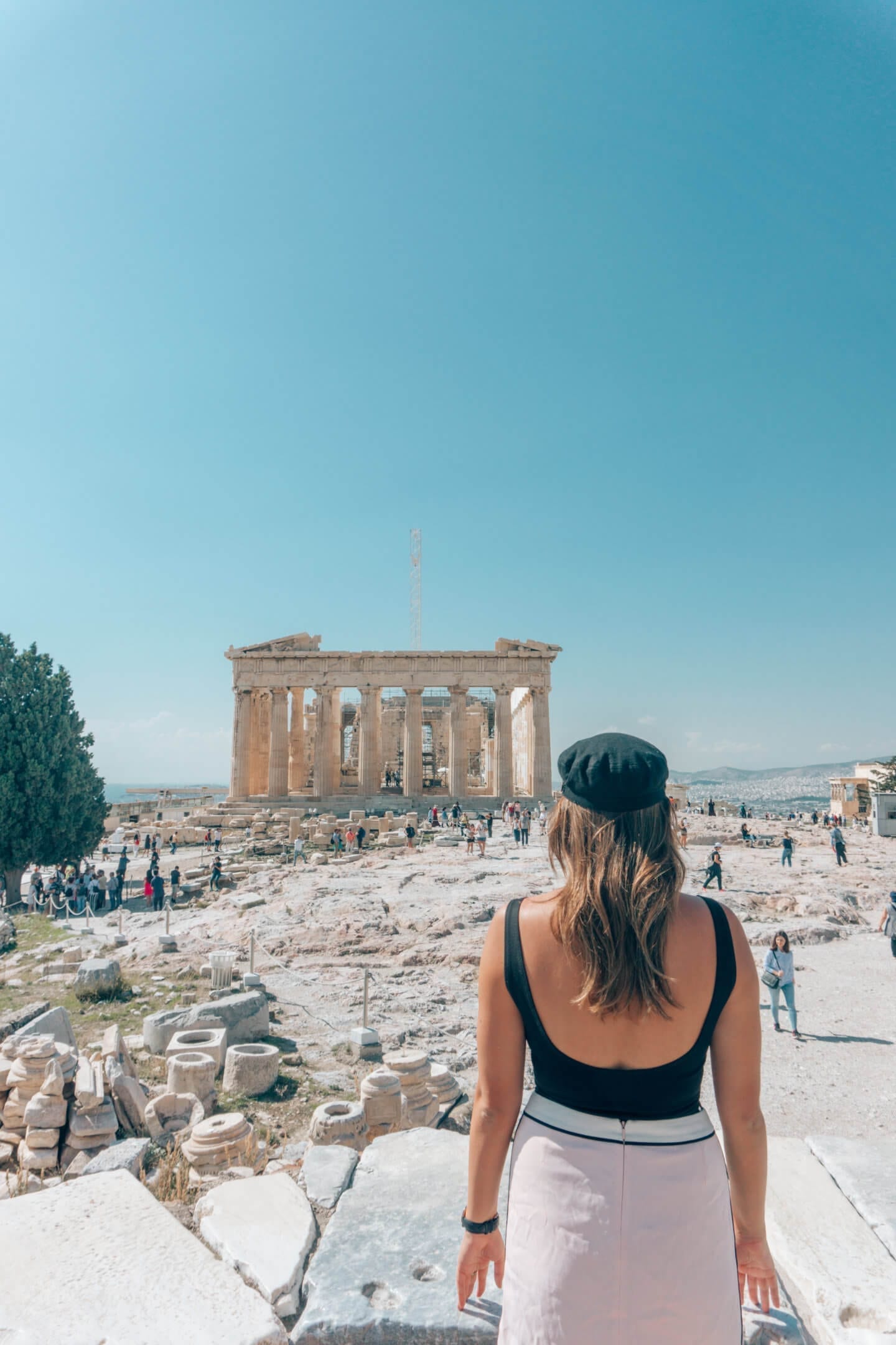 A must-see on your 10 days in Greece itinerary is the Acropolis in Athens. A girl looks at the Parthenon with her back towards us.