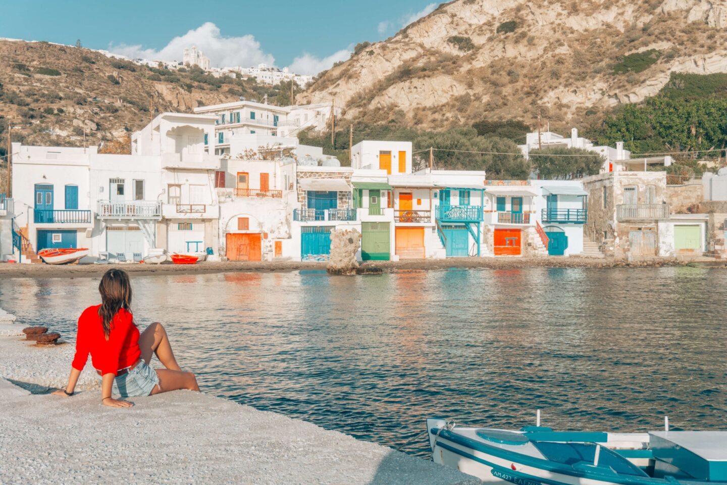 Milos Travel Guide: A girl in a red sweater sits and admires the  colourful houses of Klima.