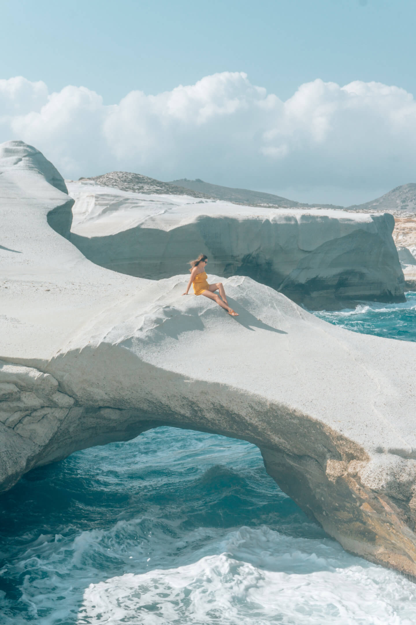 A girl sits on the moonlike archway of Sarakiniko on Milos Island in Greece. Definitely a must see beach on this Milos Travel Guide