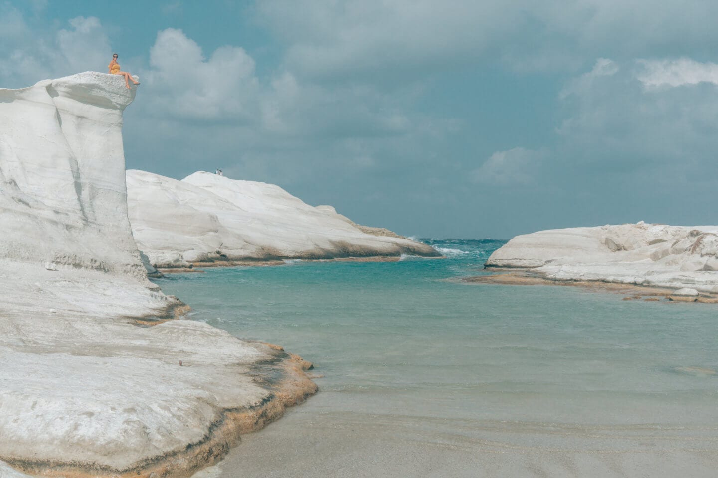 A girl sits atop an oceanside cliff at Sarakiniko Beach during this Milos travel Guide