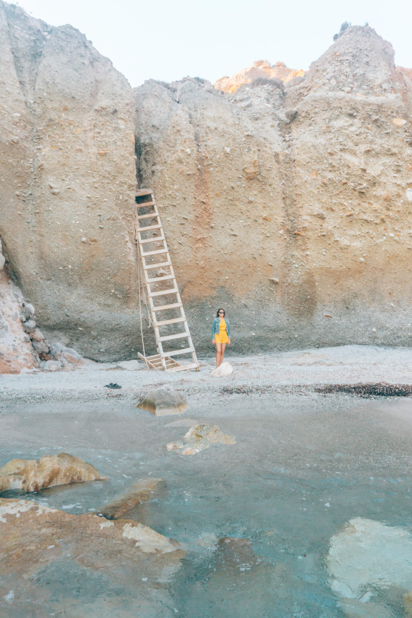 Girl standing at the bottom of the ladder at Tsigrado Beach - a must see beach on this Milos Travel Guide