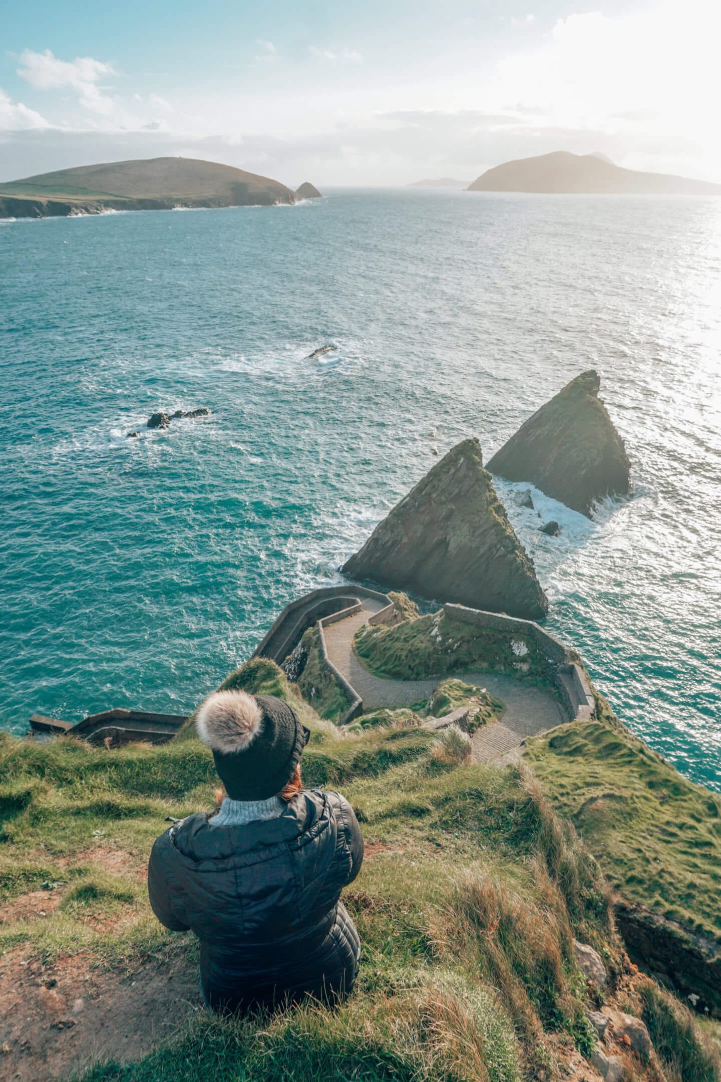 Girl sitting at Dunquin Harbour overlooking the twisting staircase and ocean