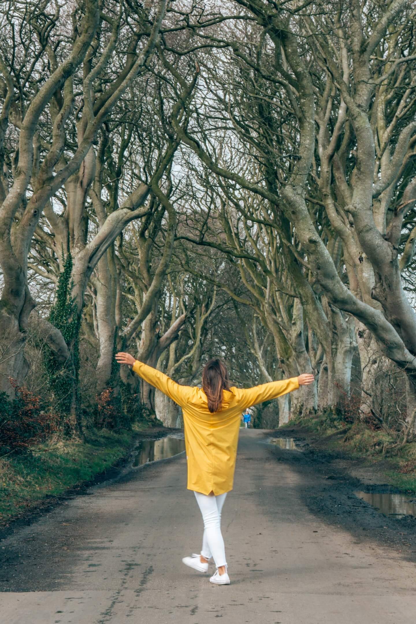 Girl in yellow jacket with hands up in front of the Dark Hedges in Northern Ireland - places to visit in Ireland