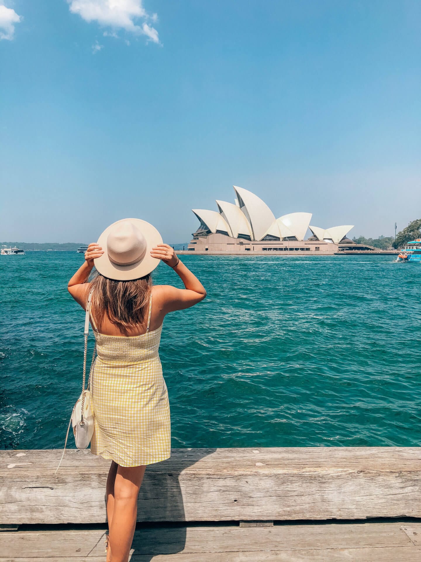 A girl wearing a hat and a yellow dress, looks out at the Sydney Opera House in Australia