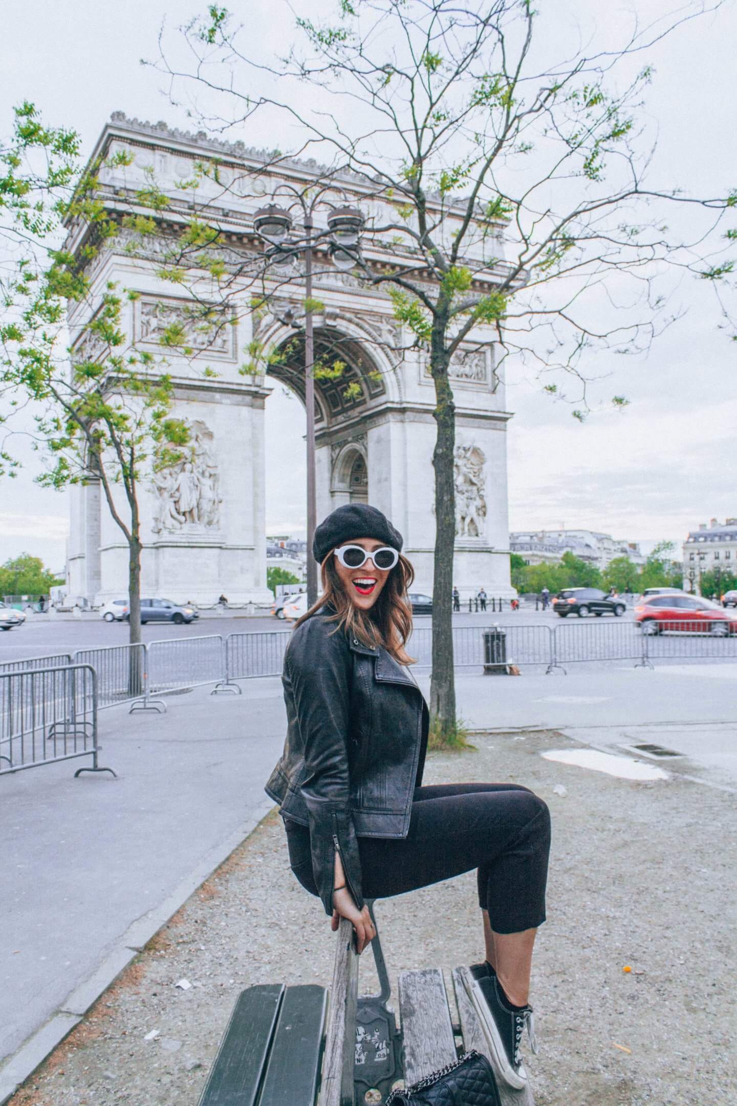 A young girl wearing all black and a beret sits in front of the Arc de Triumph in Paris, France