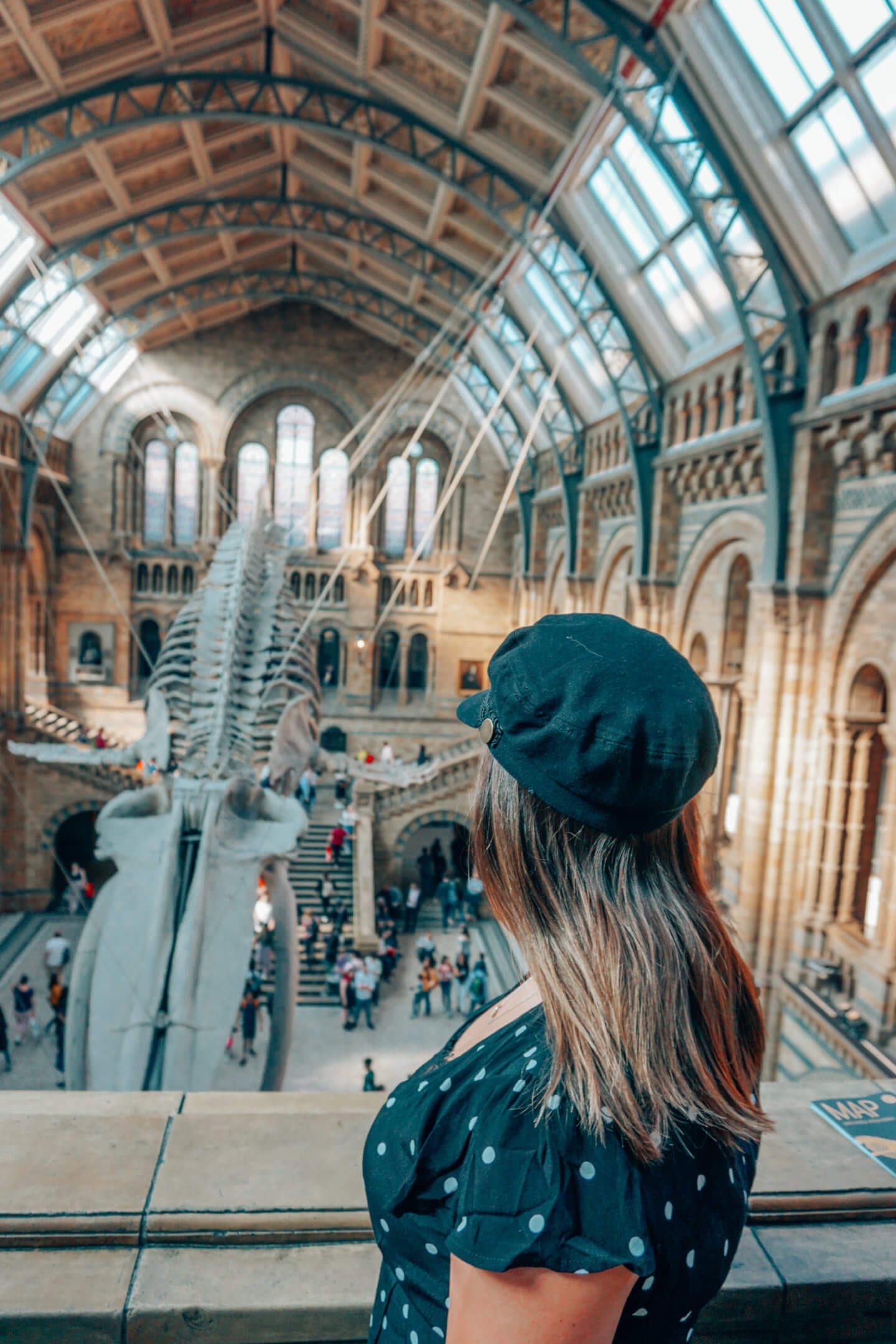 A girl wearing a black hat looks out at a skeleton of a whale in the British Museum in London