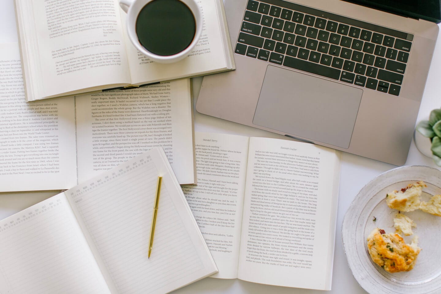 A cup of coffee on top of a bunch of books with a laptop open to virtually travel the world at home