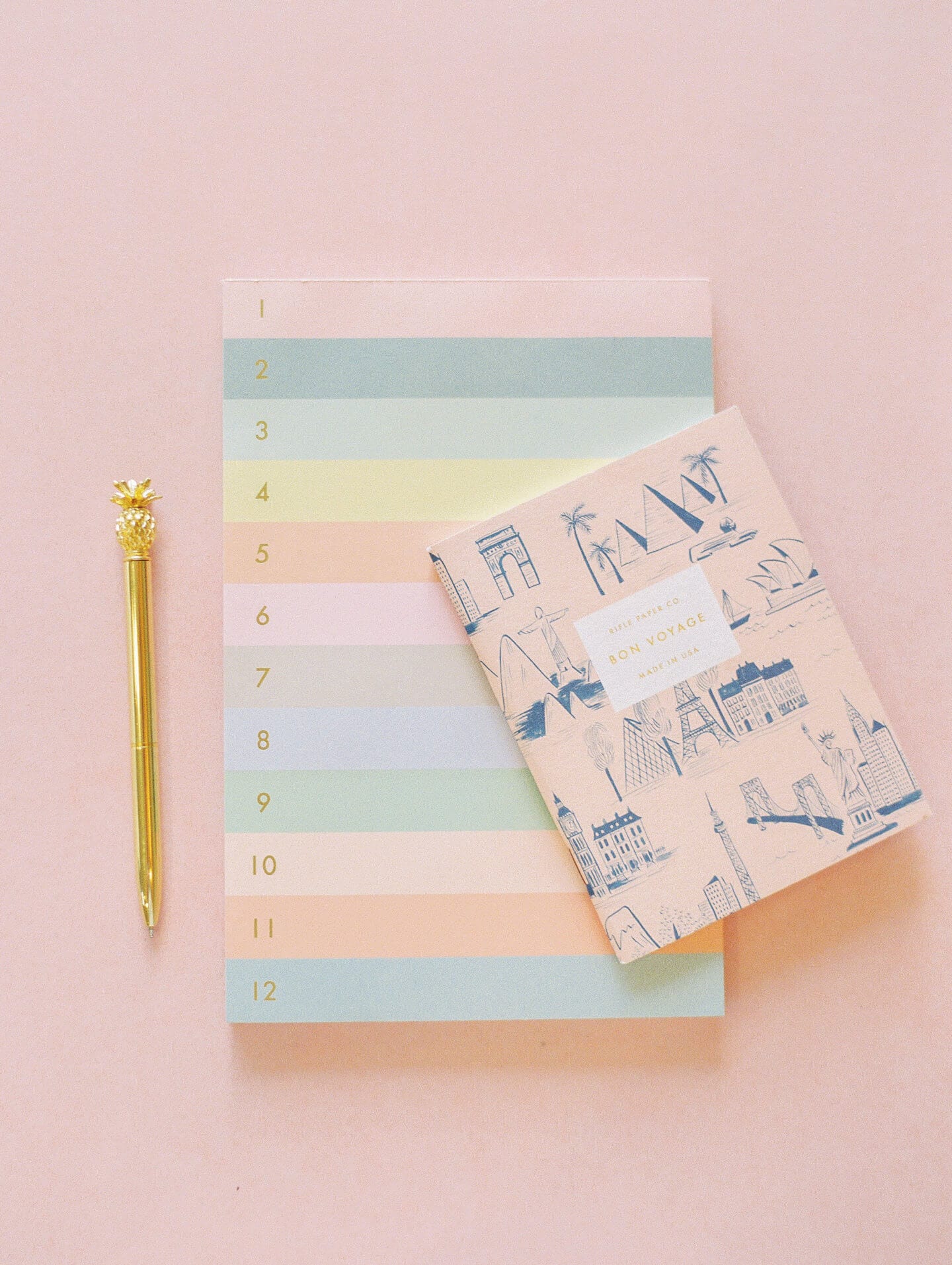 Two colourful notebook and a gold pen on a pink desk