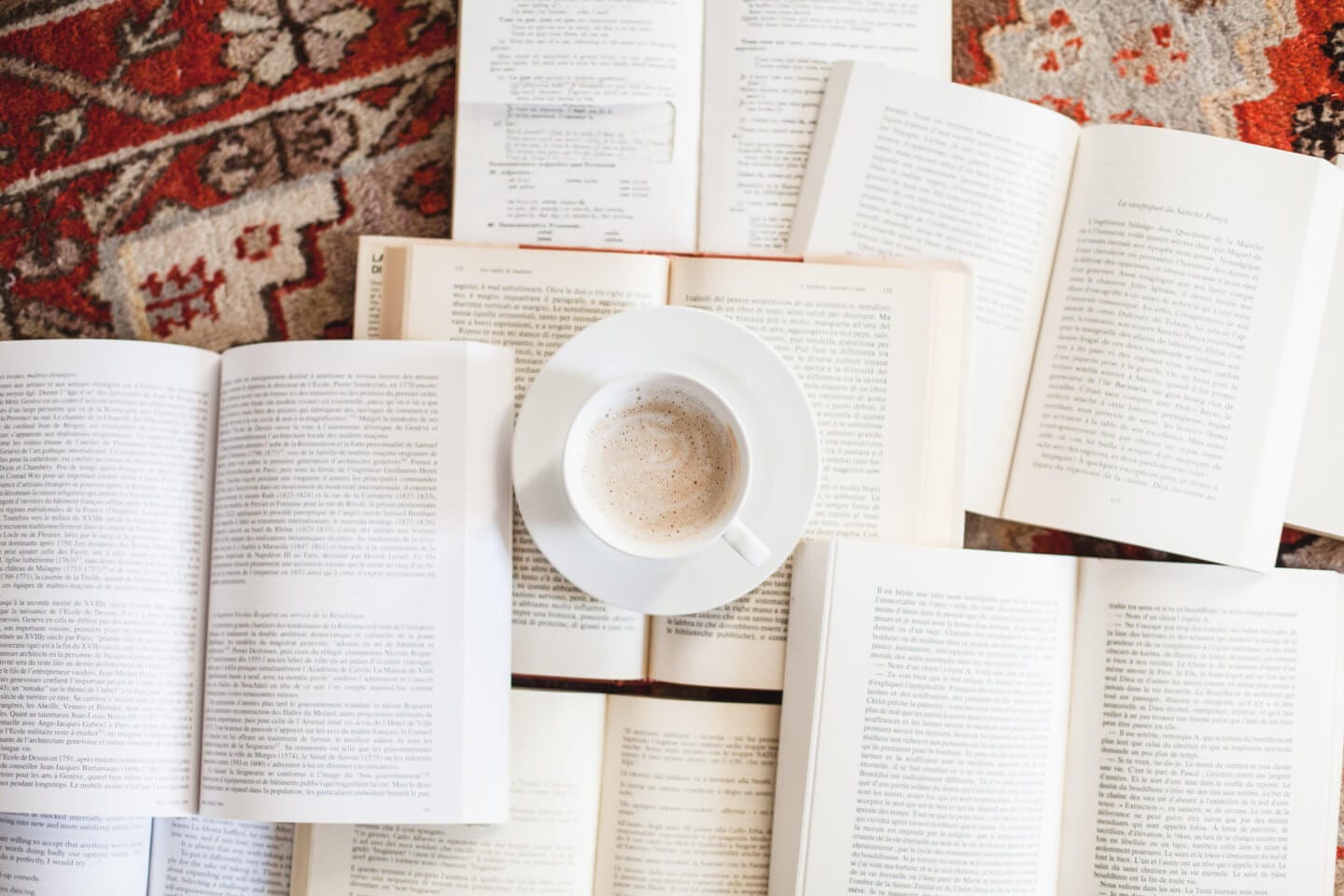 A coffee on top of a stack of travel books on a red carpet