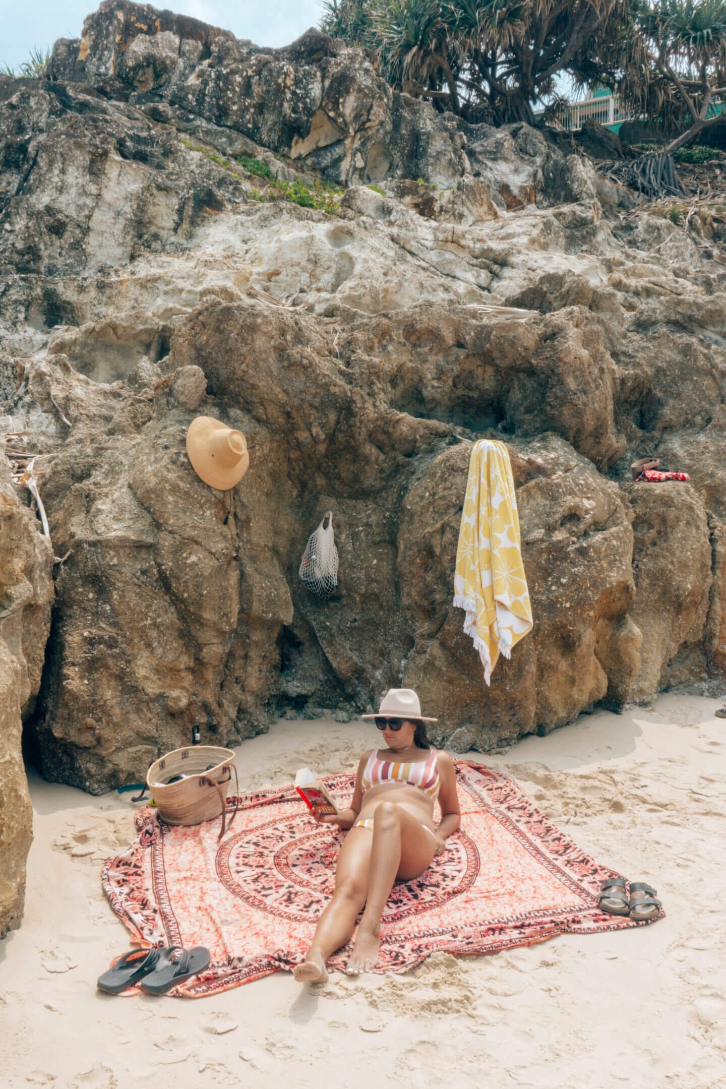 Girl sits and reads a book on the beach with rocks in the background