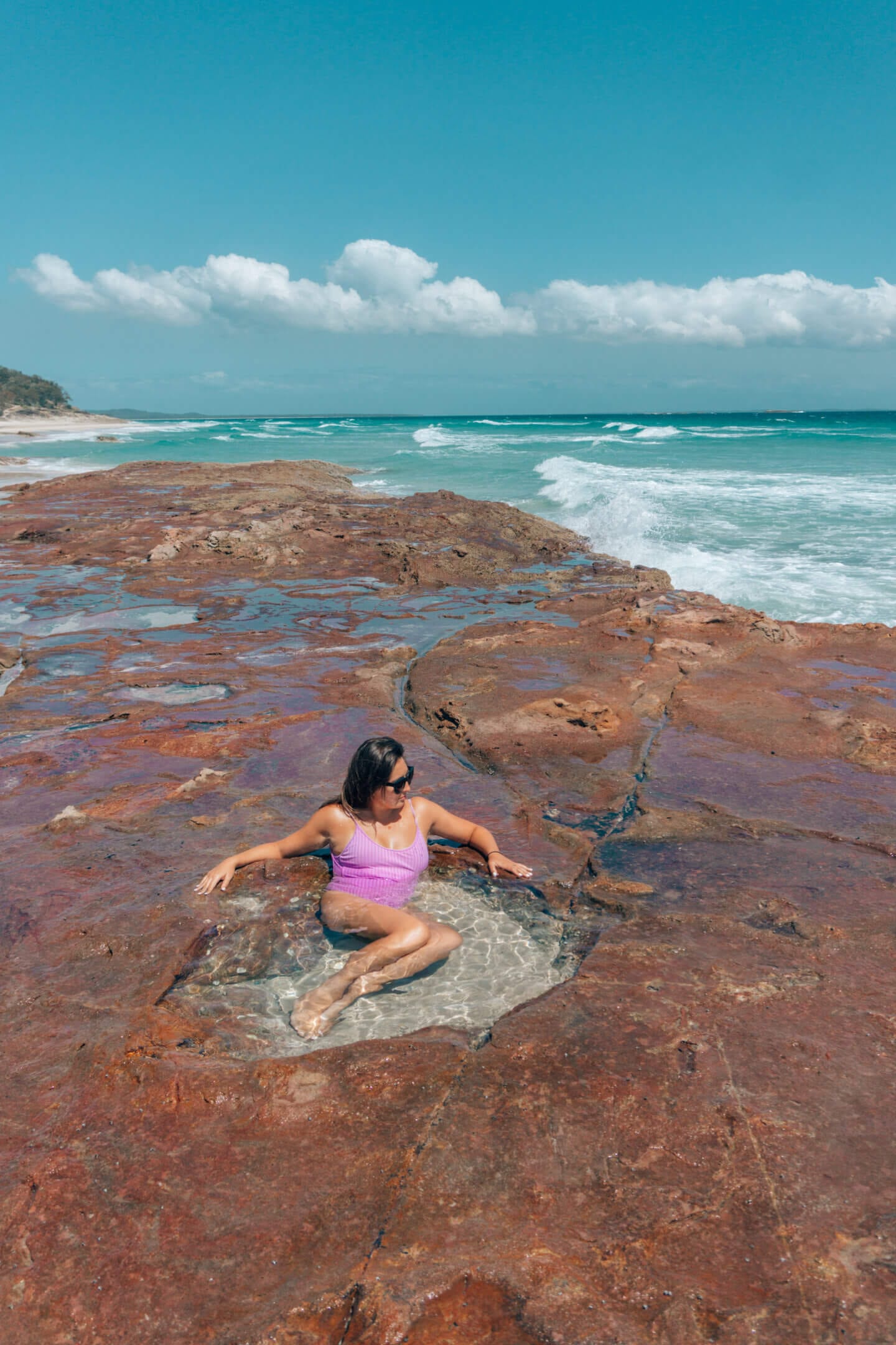 A girl in a purple bathing suit sitting in a rock pool on North Stradbroke Island