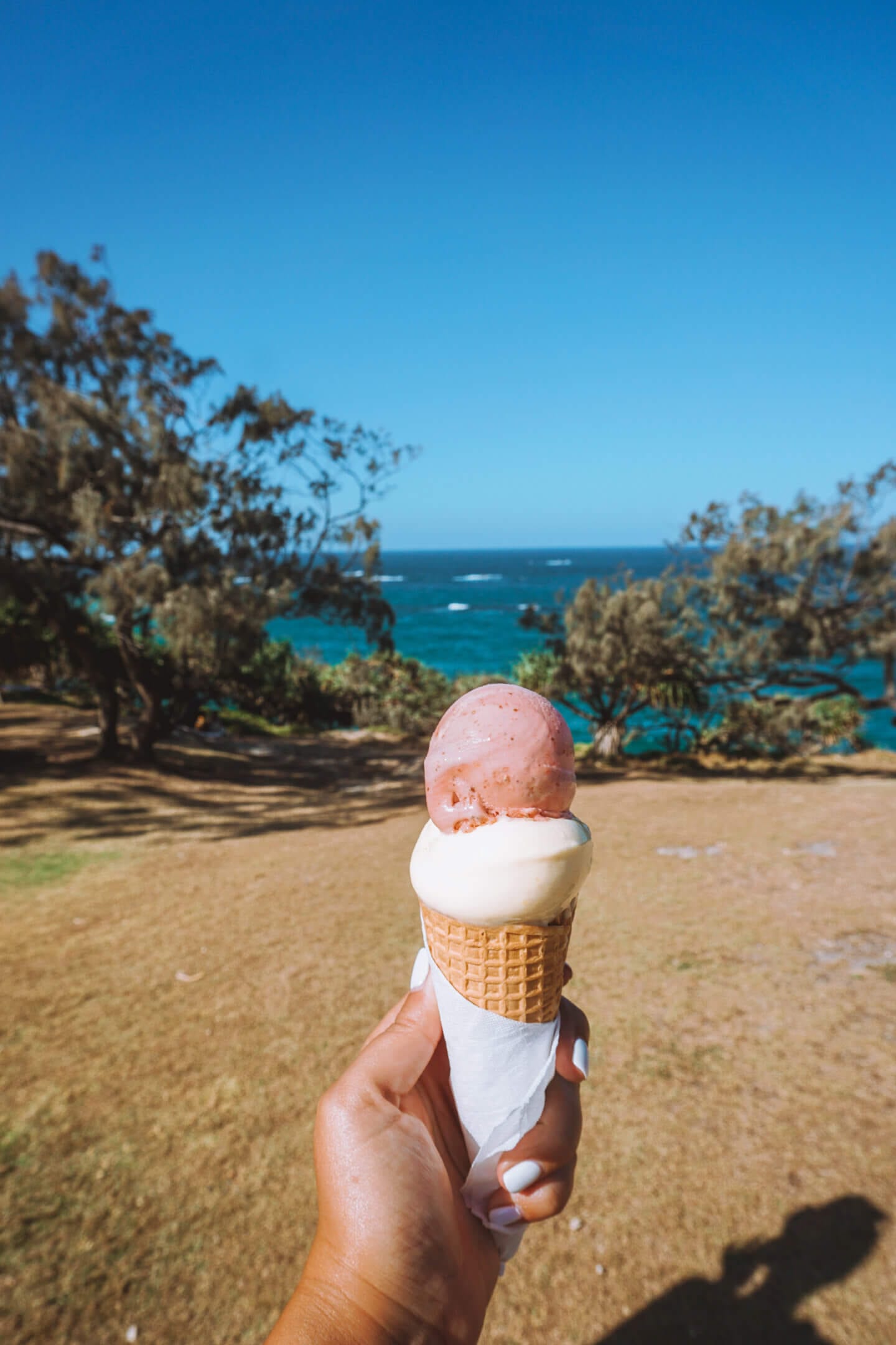 Person holds a Oceanic Gelato cone with two scoops of ice cream and the ocean in the background