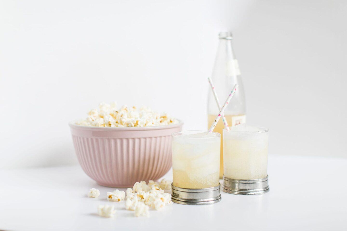 A pink bowl filled with popcorn and two glasses of soda pop: the best travel movie snacks