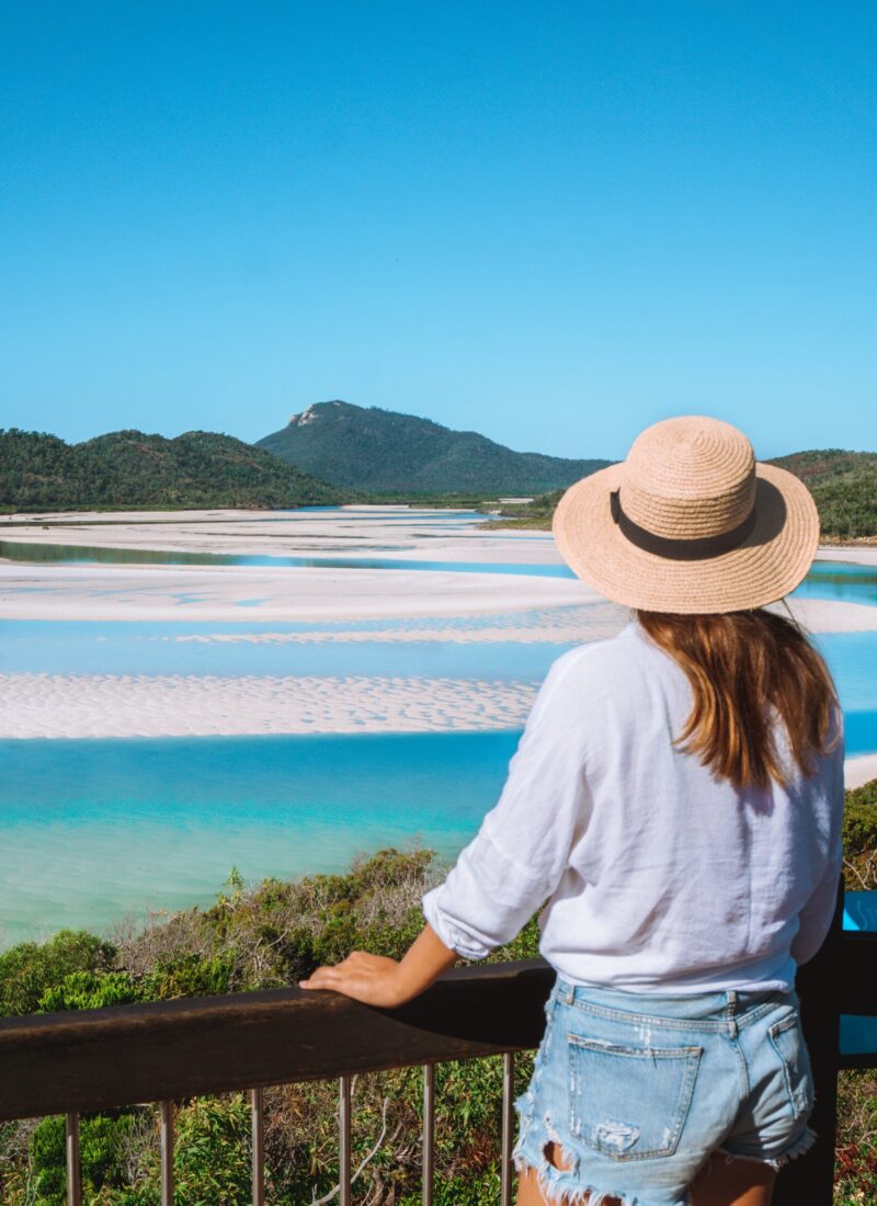 A girl with a hat looks out at Whitehaven Beach at the lookout during low tide