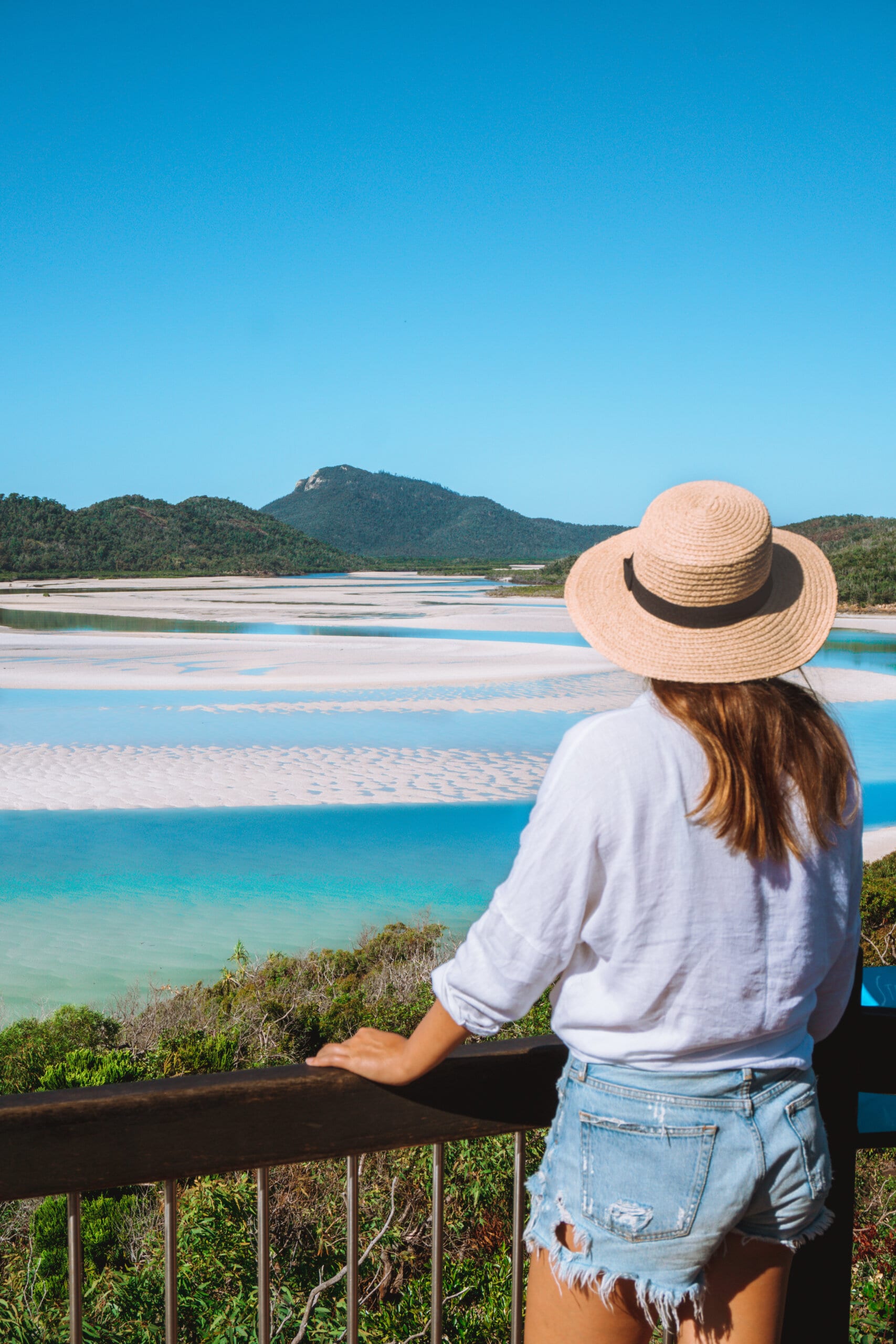 A girl with a hat looks out at Whitehaven Beach at the lookout during low tide