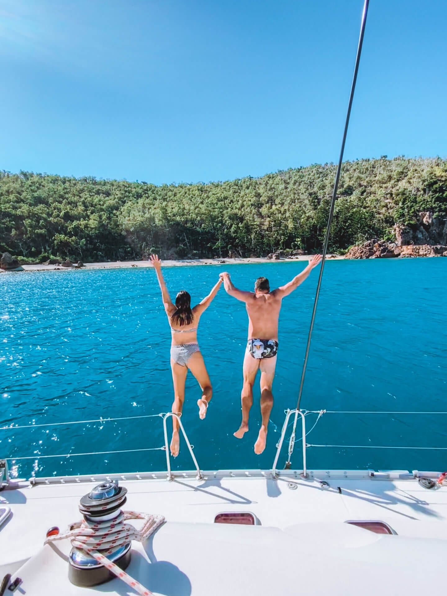 A couple jumps off a boat into the blue waters of the Whitsundays