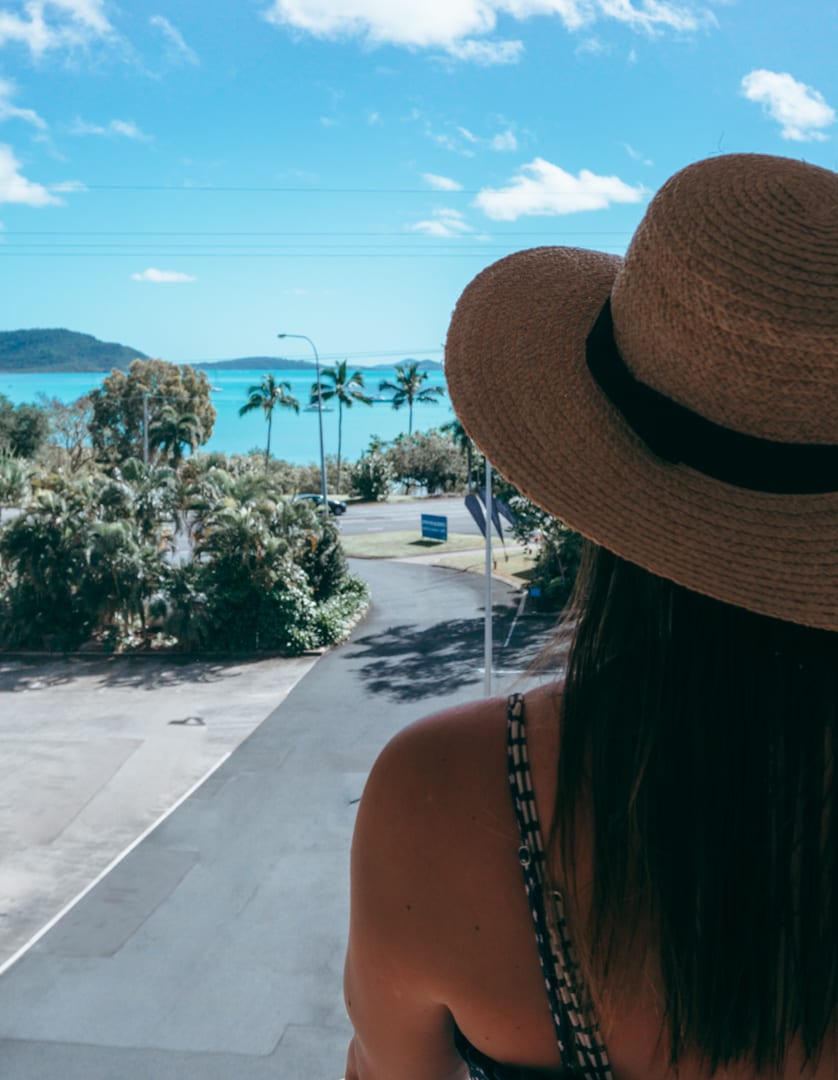 Girl with a hat on looks out towards the ocean in Airlie Beach at her hotel 