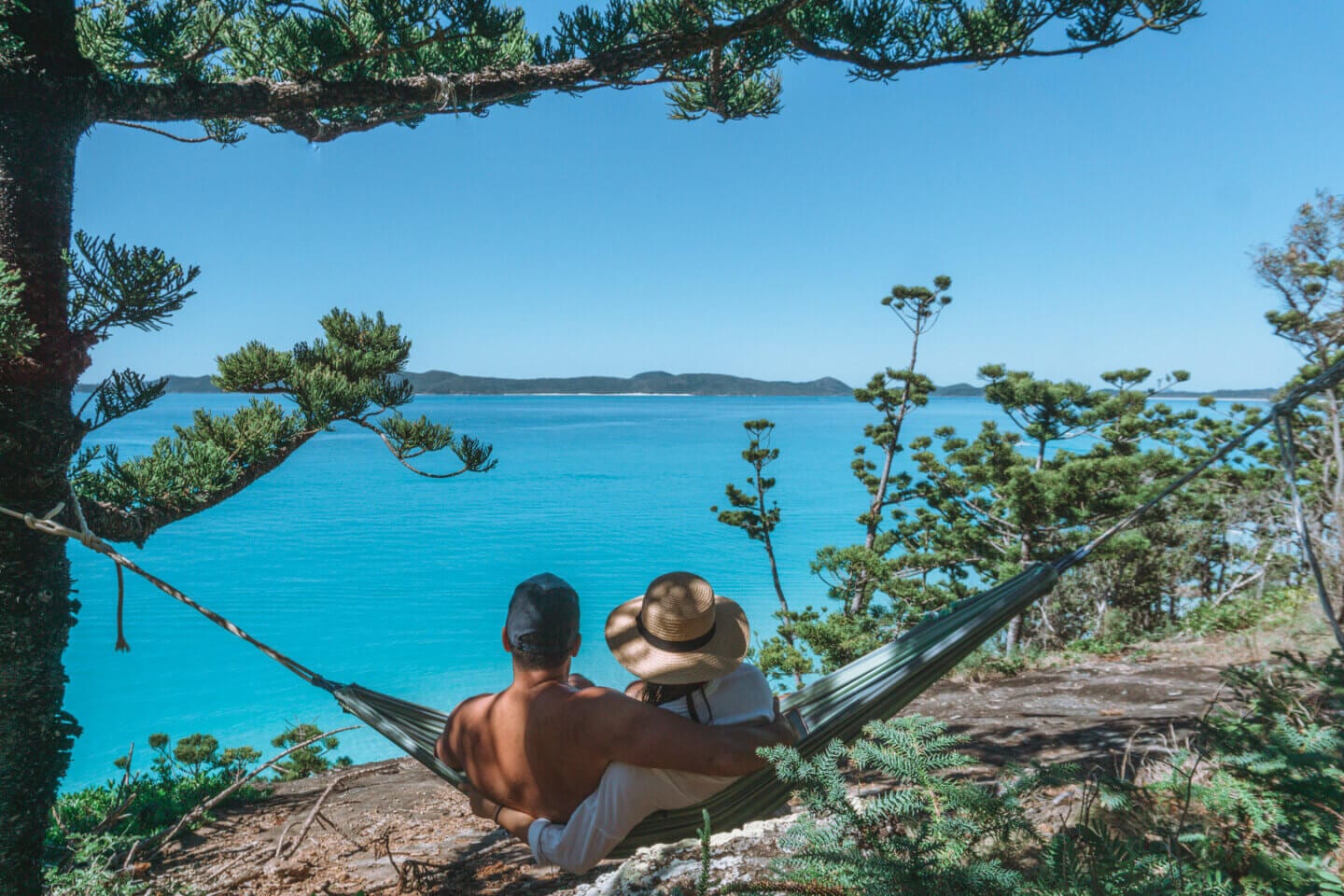 A couple with hats on lookout towards Whitehaven Beach from a hammock