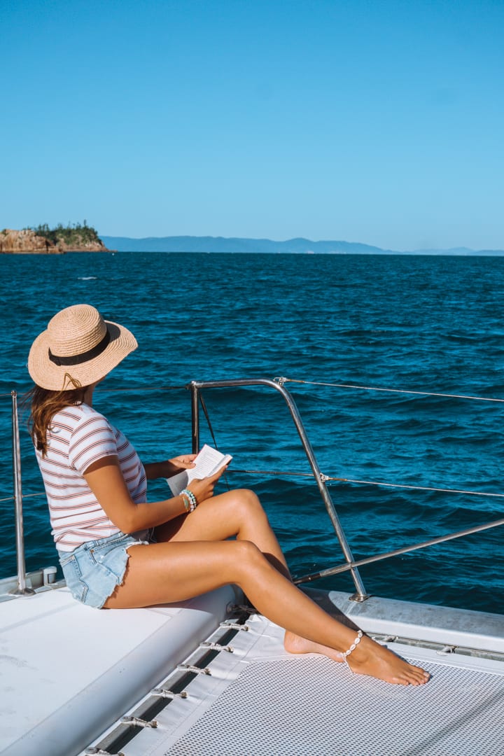 A girl with a hat on reads a book on board a sail boat