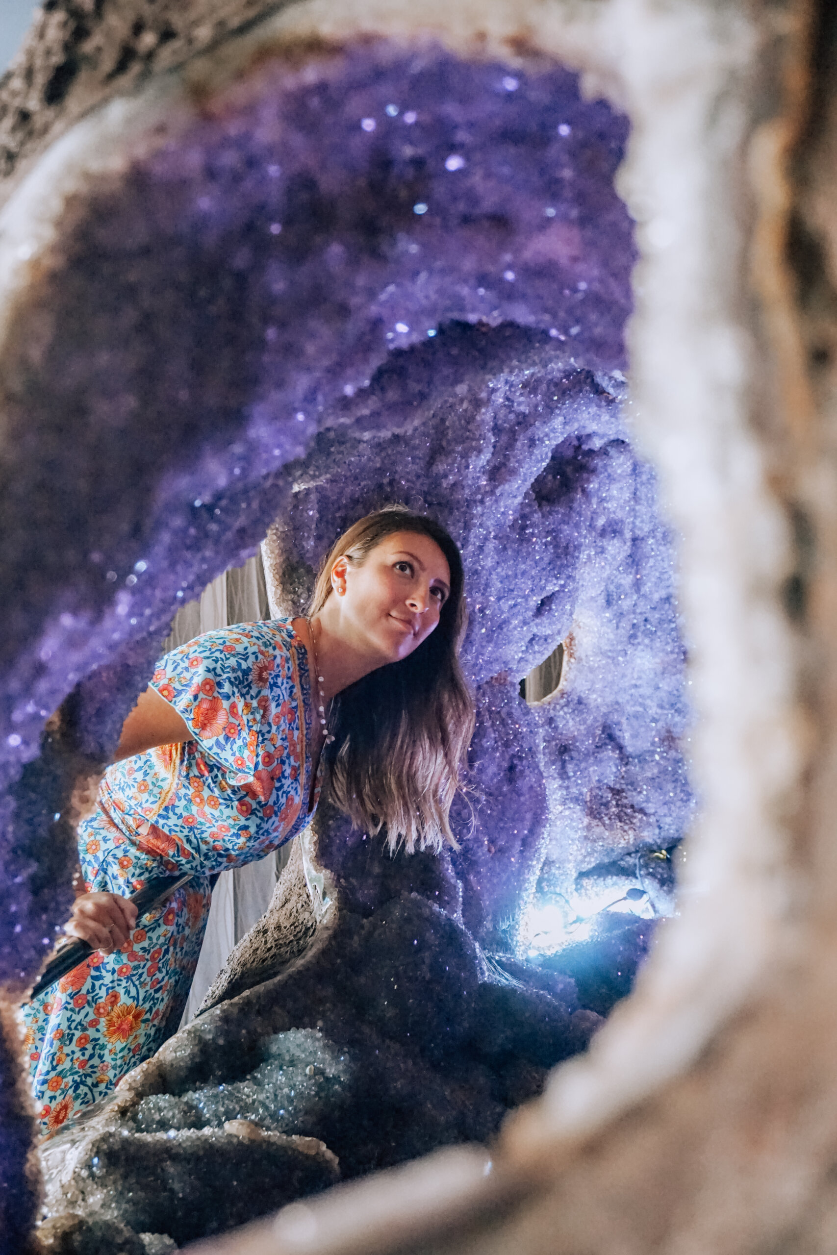 A girl wearing a blue dress looks up in an amethyst crystal cave at Crystal Castle in Mullmbimby NSW