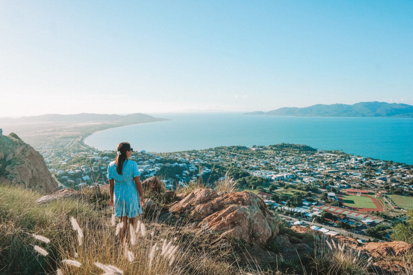 Girl in a blue dress stands on top of Castle Hill and looks down to Townsville below