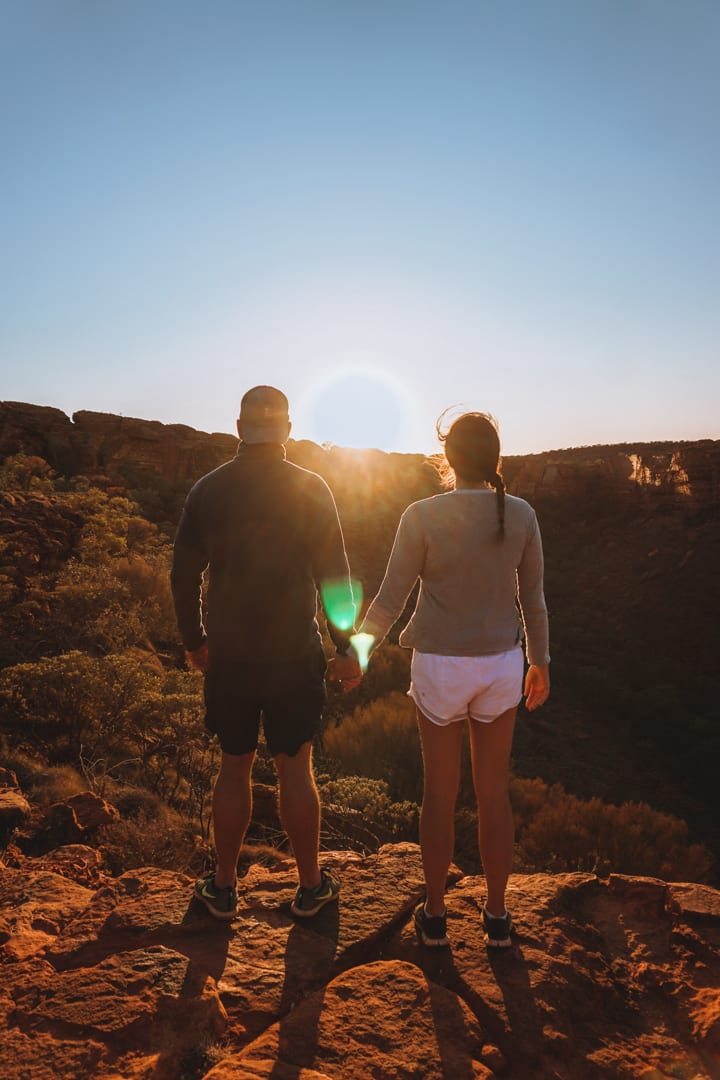 A couple stand hand in hand watching sunrise at the top of Kings Canyon
