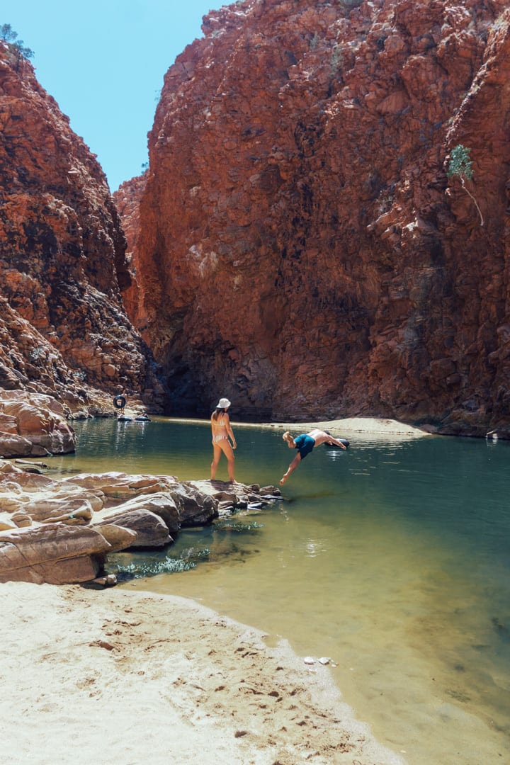 A man dives in the green water at Redback Gorge while a girl stands and watches