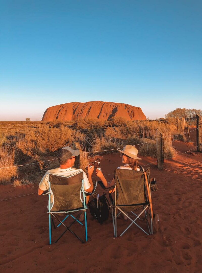 A couple in camping chairs cheersing beers during sunset at Uluru's dune lookout