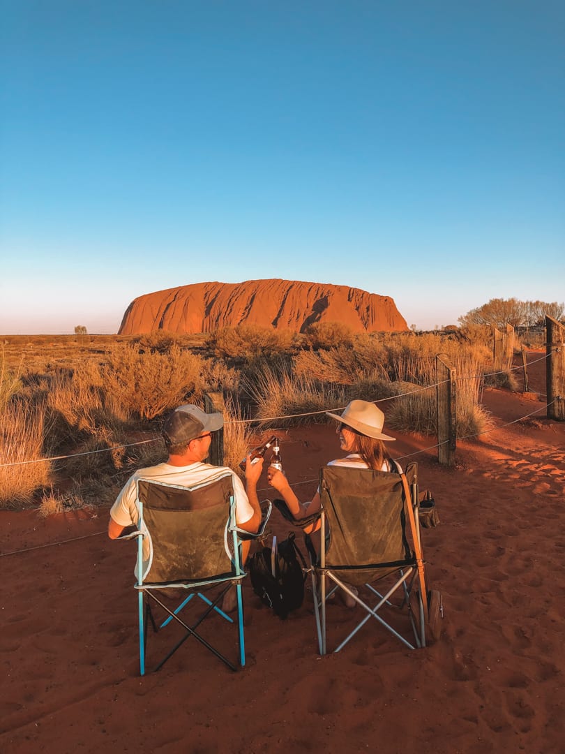 A couple in camping chairs cheersing beers during sunset at Uluru's dune lookout