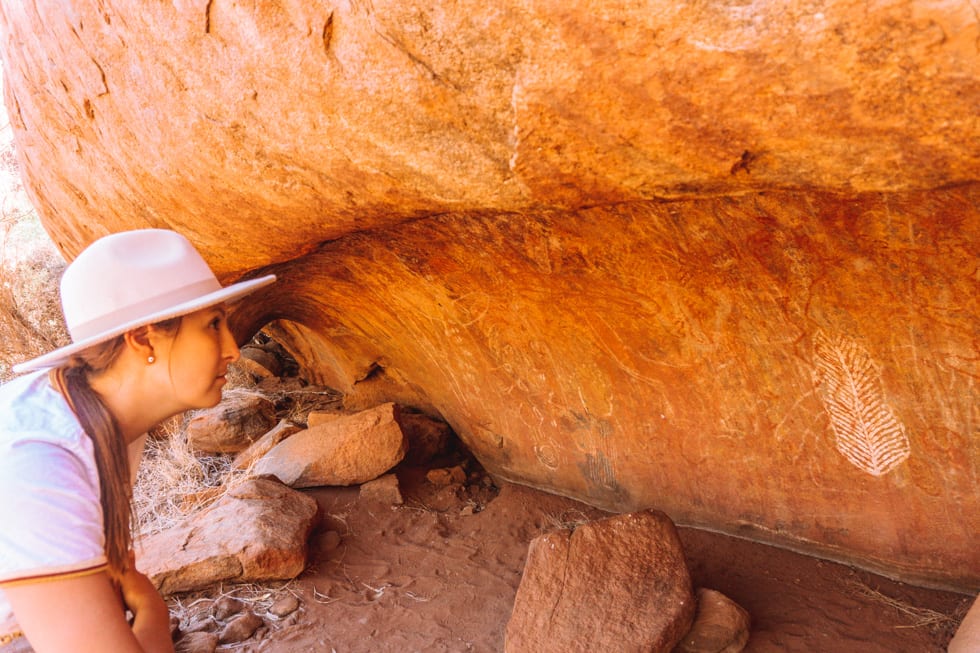 Girl with a hat on looks at ancient Aboriginal rock art at Uluru in Northern Territory, Australia