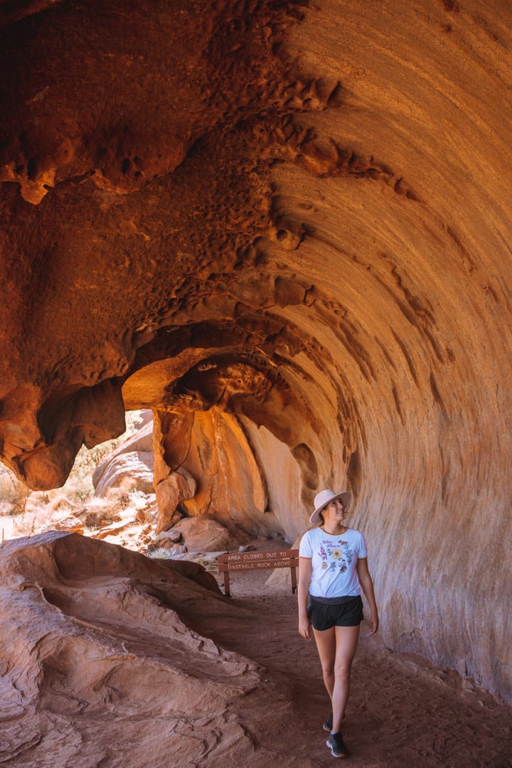 Girl with a hat does the base walk in Uluru and walk beneath a cave