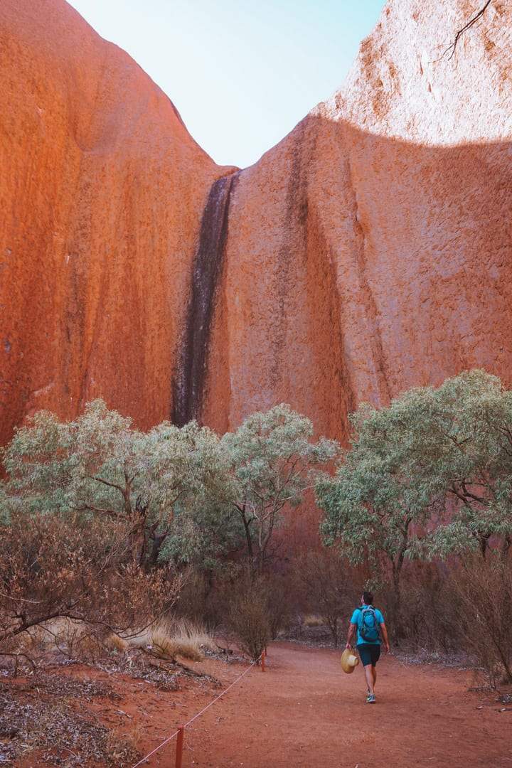 Man with a blue shirt walks towards the sacred watering hole at Uluru