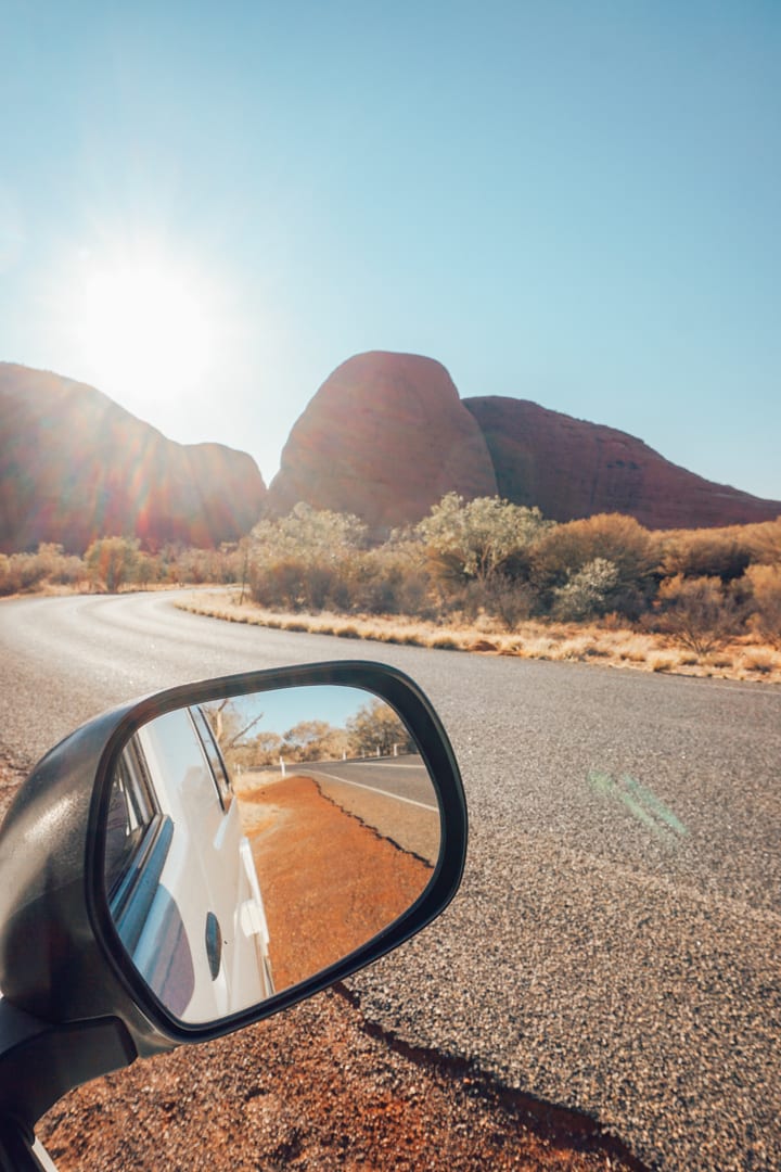 Alice Springs to Uluru: Road to Kata Tjuta with car rearview mirror in the foreground