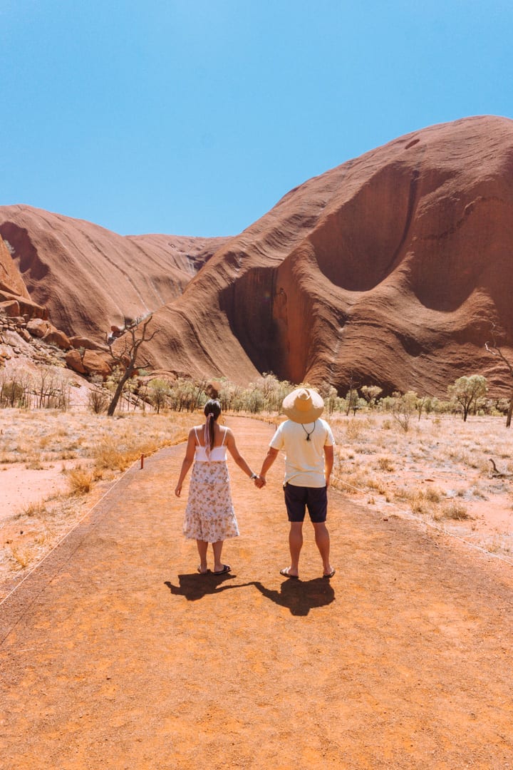 A couple stand hand in hand looking at Uluru