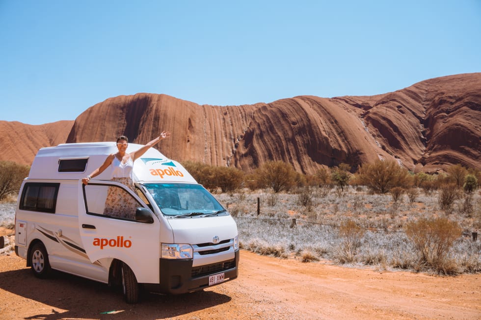 Girl stands in an Apollo campervan during a road trip from Alice Springs to Uluru.