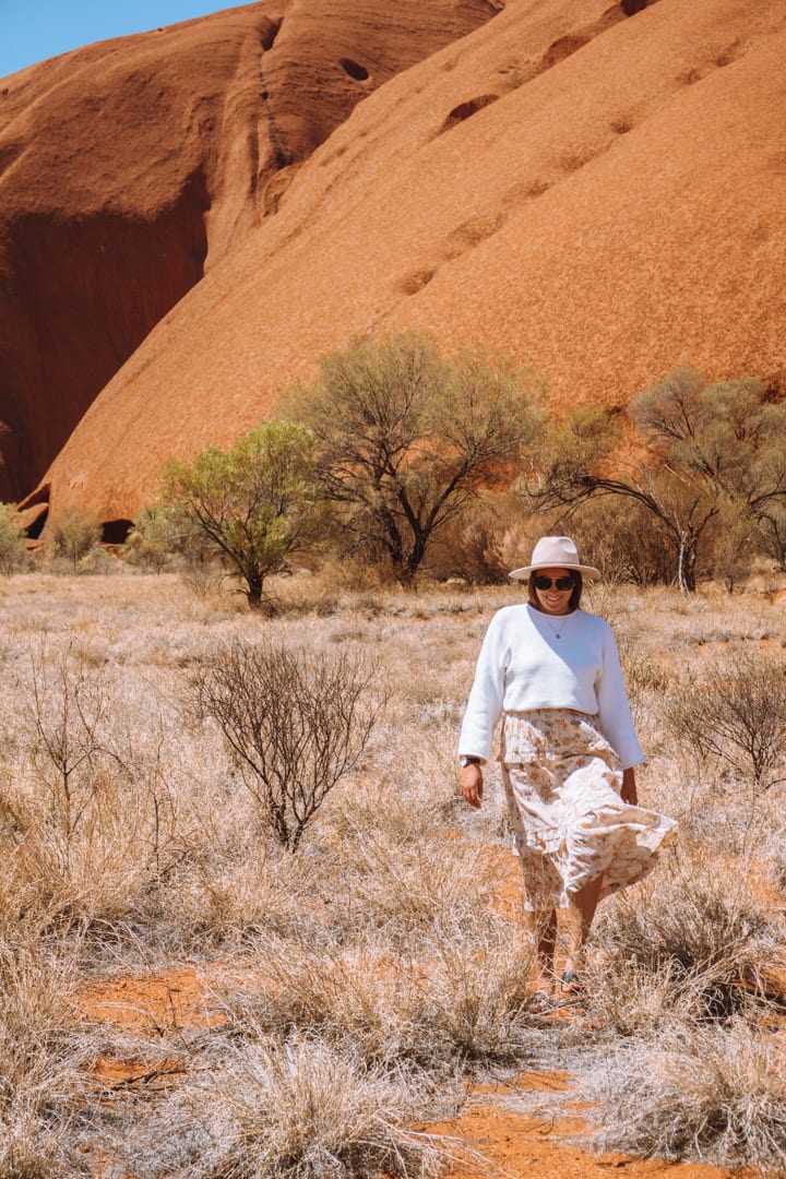 Alice Springs to Uluru Road trip: Girl with a hat on walks through the bush at the base of Uluru