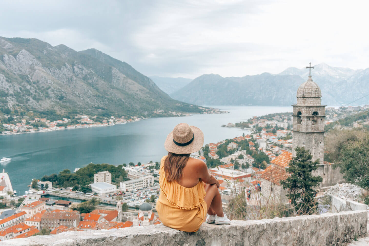The girl with a hat on sits and admires the view of Kotor in Montenegro - one of the most romantic places in Europe for a Unique Honeymoon