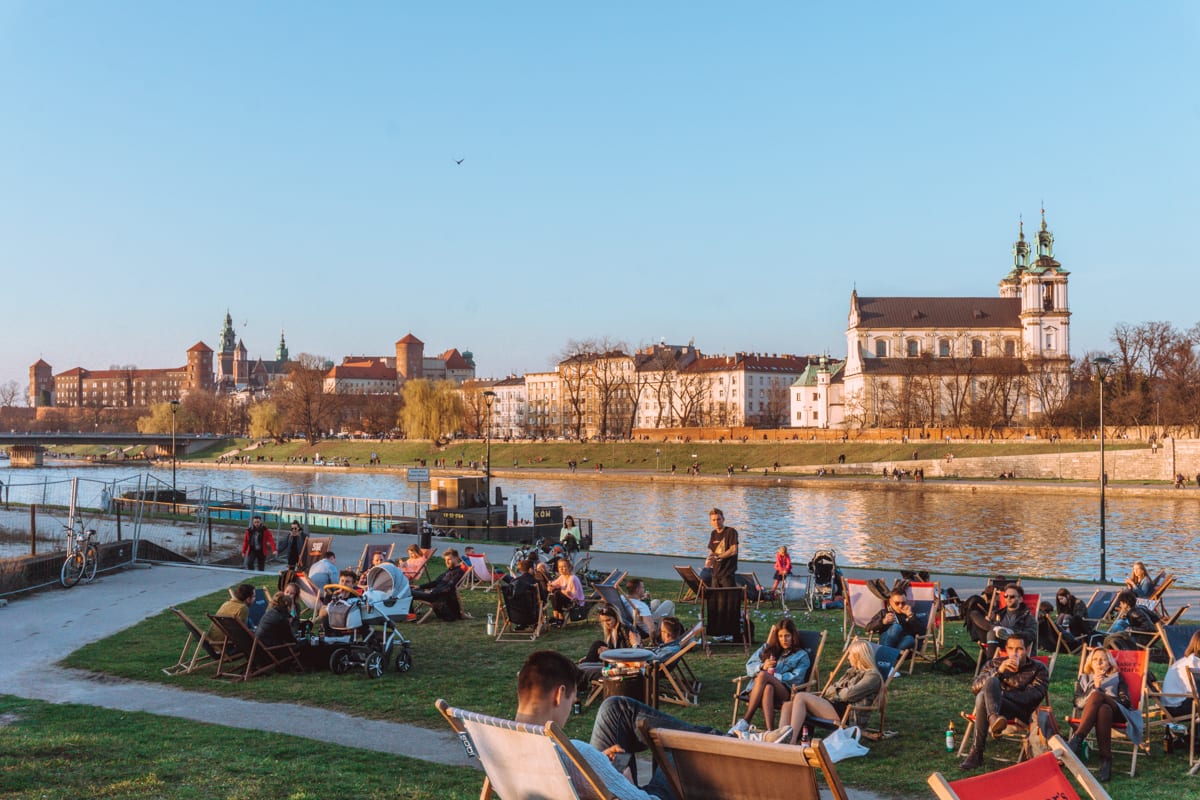 Best Places for Digital Normads: Young people enjoy the sites and sun of Krakow, Poland along the riverfront at Forum Przestrzenie