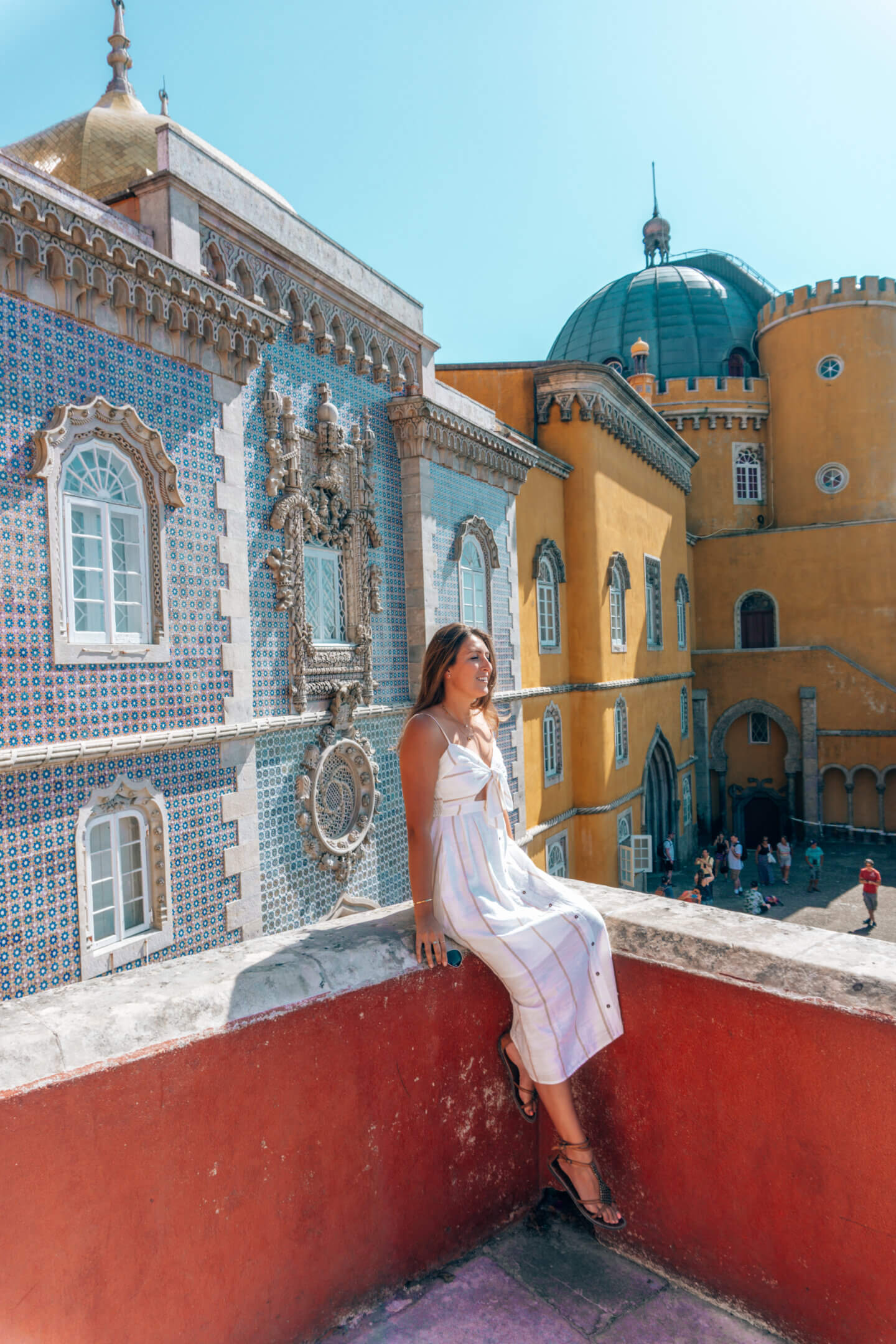 A girl sits on a ledge in front of Pena Palace, in Sintra, Portugal