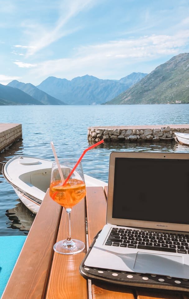 Best places for digital nomads: A laptop on a table with an Aperol Spritz with Montenegro mountain and ocean views in the background.