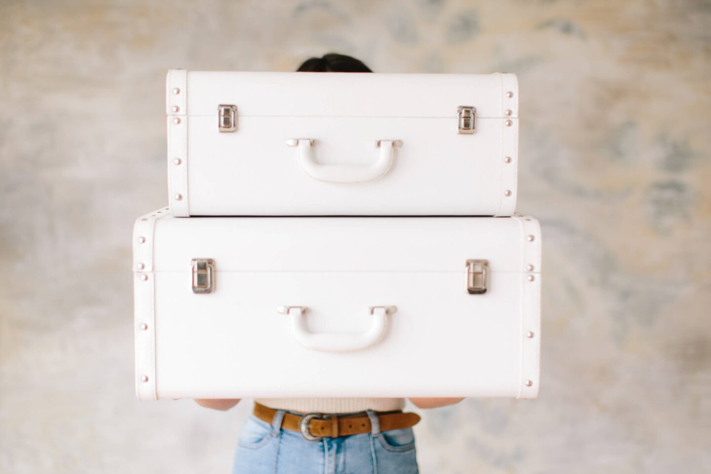 A women wearing blue jeans hold two vintage white suit cases. Travel packing tips!