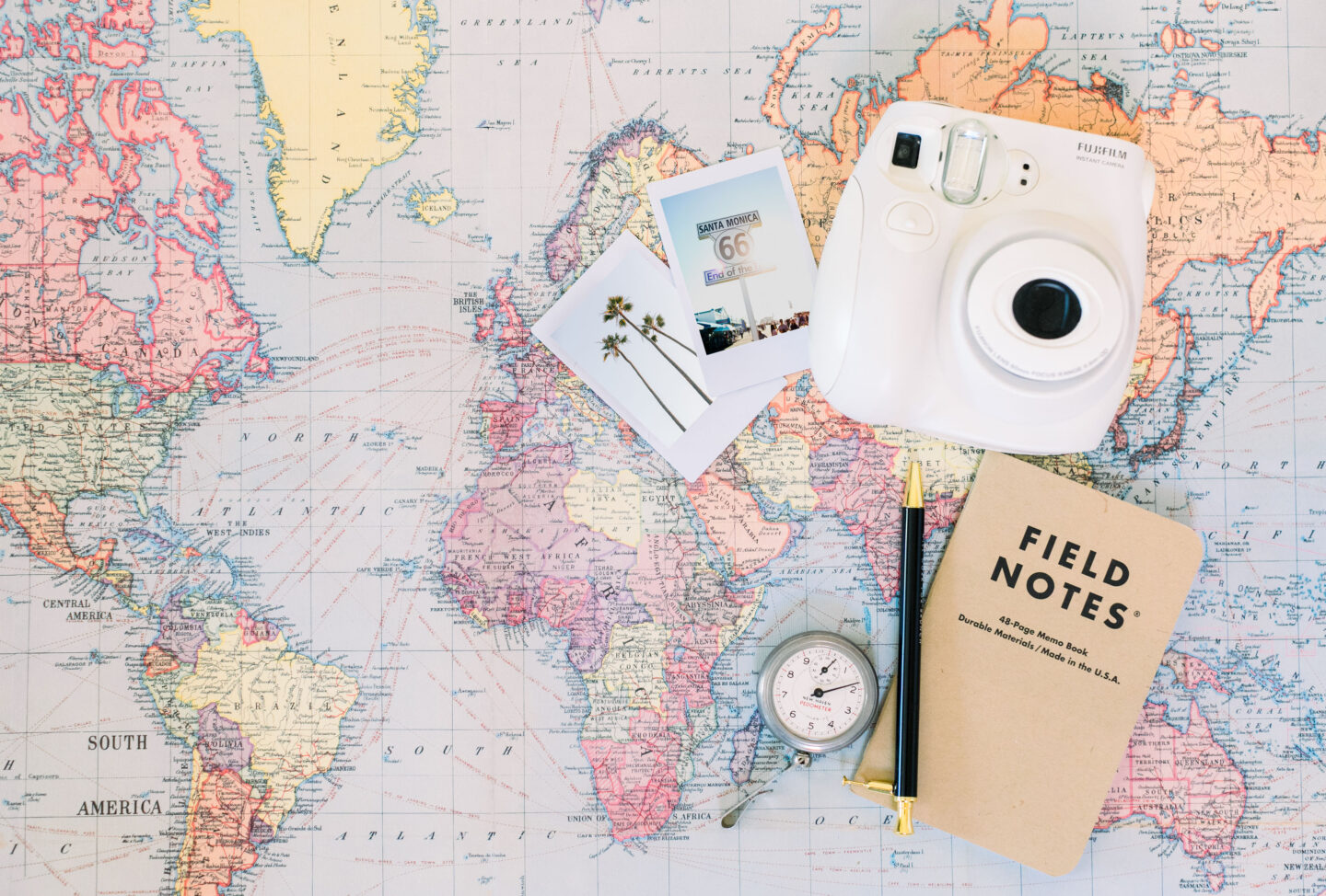 A world map with a Polaroid camera, photos and a journal used to make travel planning a breeze with my top travel resources. 